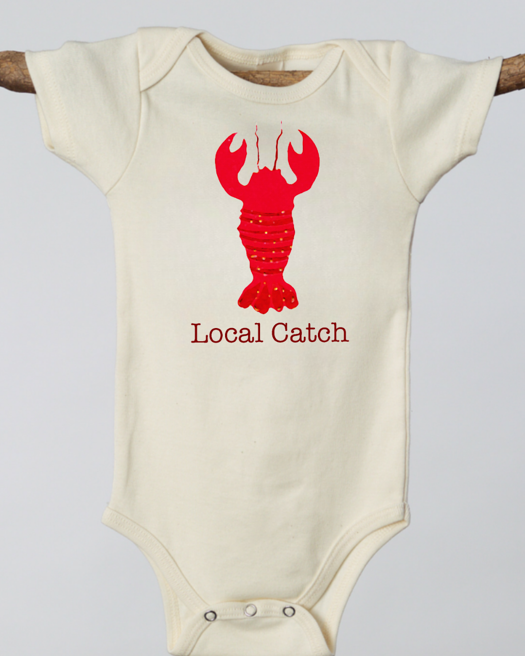 Beige baby onesie with red lobster graphic and 'Local Catch' text on a light gray background