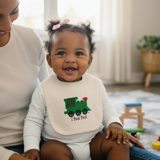 Black baby girl wearing I Toot Toot train bib with white romper