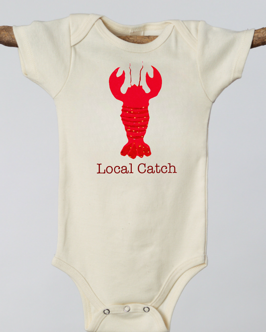 Beige baby onesie with red lobster graphic and 'Local Catch' text on a light gray background